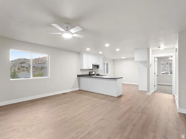 Kitchen featuring a peninsula, open floor plan, dark countertops, ceiling fan, and white cabinets