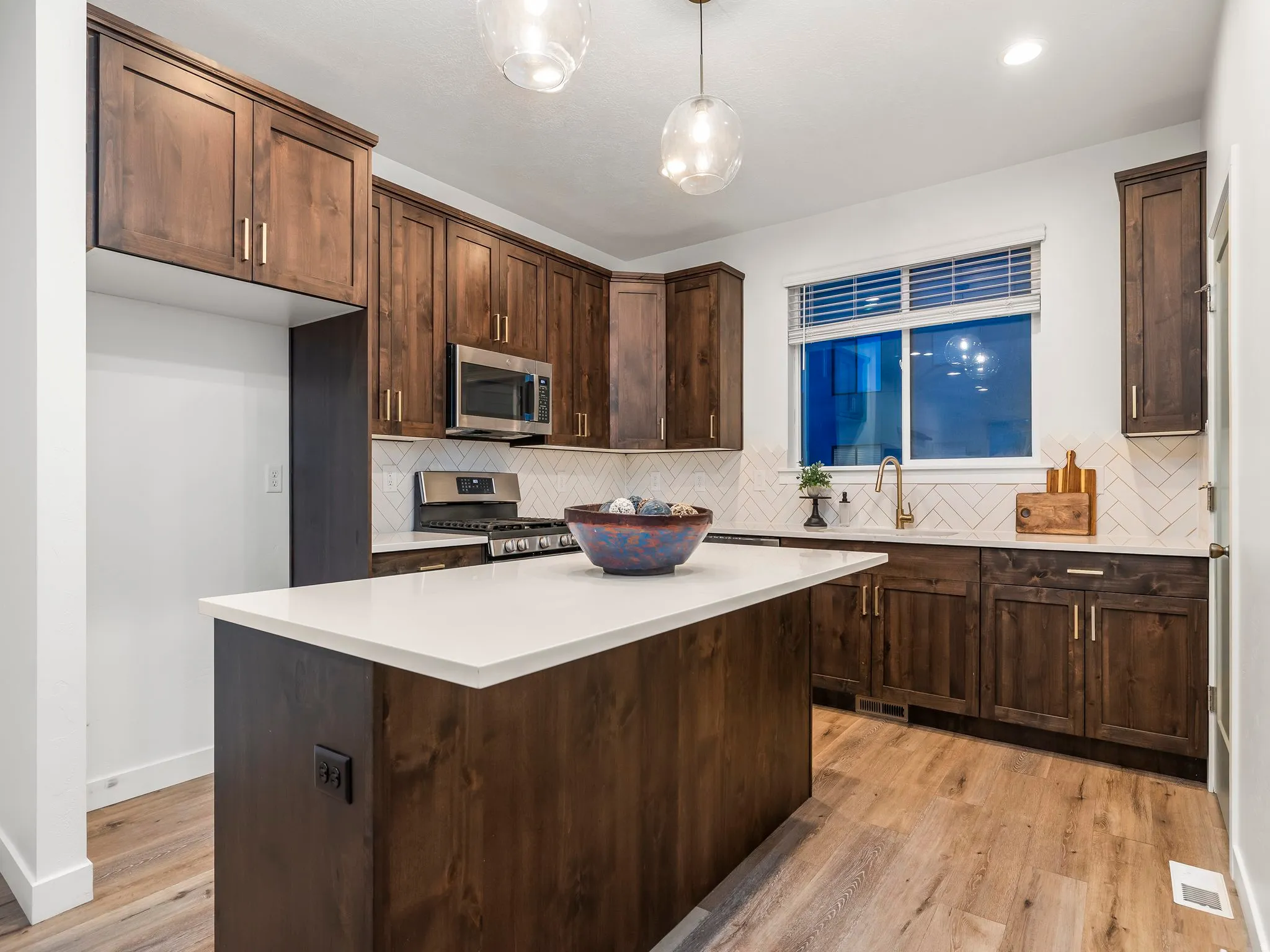 Kitchen with dark wood finish cabinetry, stainless steel appliances, light wood-style floors, a kitchen island, and decorative light fixtures