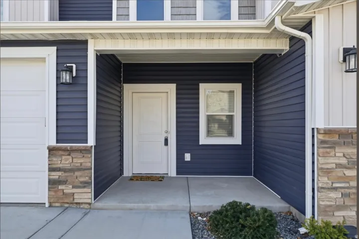 View of exterior entry featuring covered porch, stone siding, and a garage
