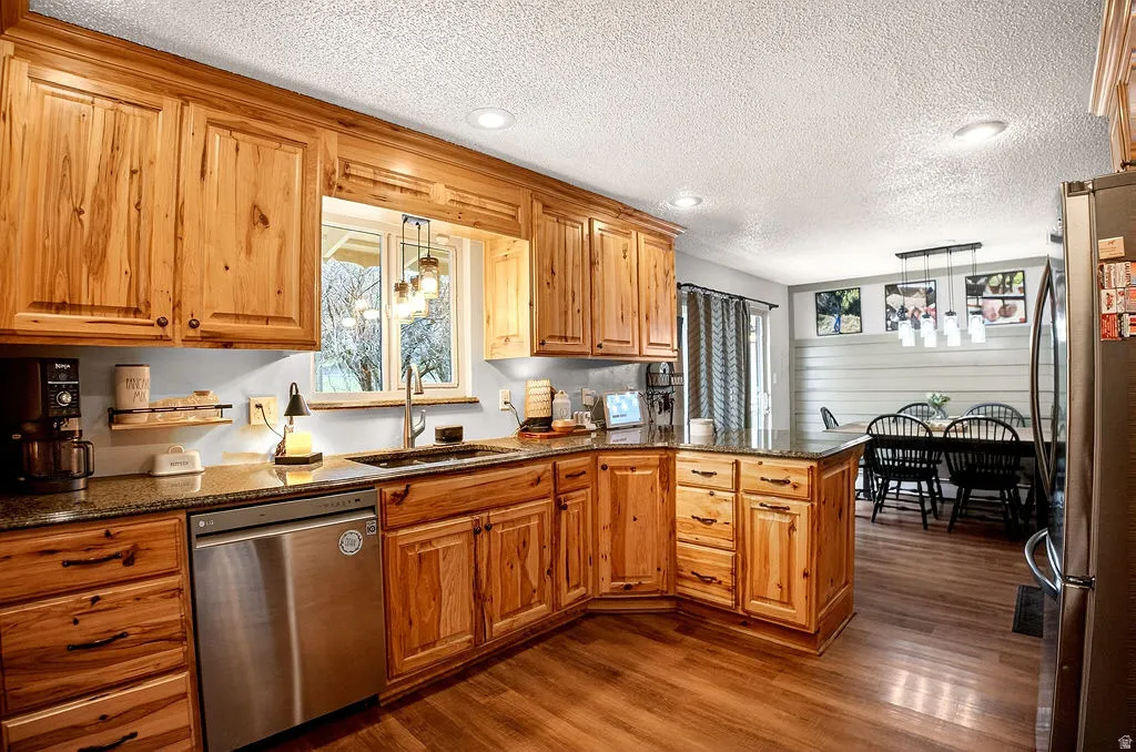 Kitchen featuring dark stone countertops, stainless steel appliances, a textured ceiling, wood finish cabinetry, and a peninsula