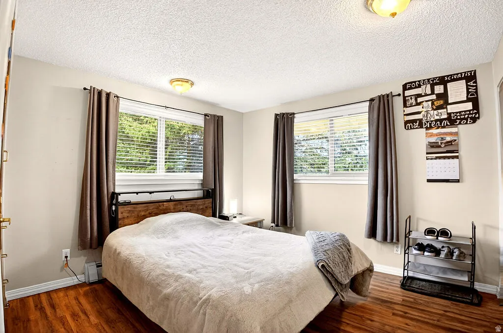 Bedroom featuring dark wood-style floors, a textured ceiling, multiple windows, and a baseboard radiator