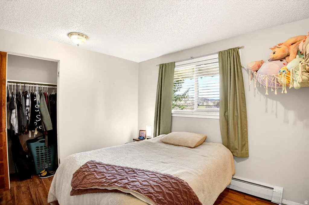 Bedroom featuring a baseboard radiator, a closet, a textured ceiling, and wood finished floors