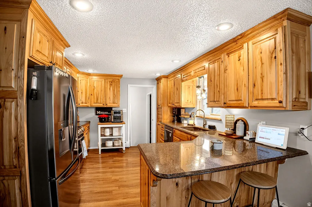 Kitchen featuring recessed lighting, black refrigerator with ice dispenser, dark stone countertops, a peninsula, and a breakfast bar area