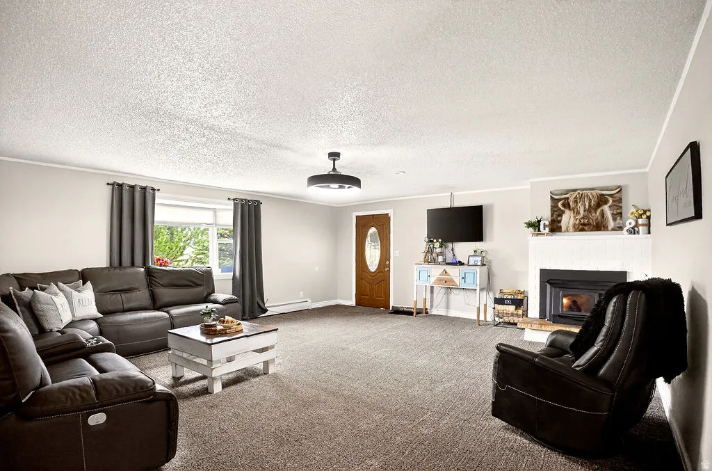 Living room featuring ornamental molding, carpet, a brick fireplace, a textured ceiling, and a baseboard heating unit