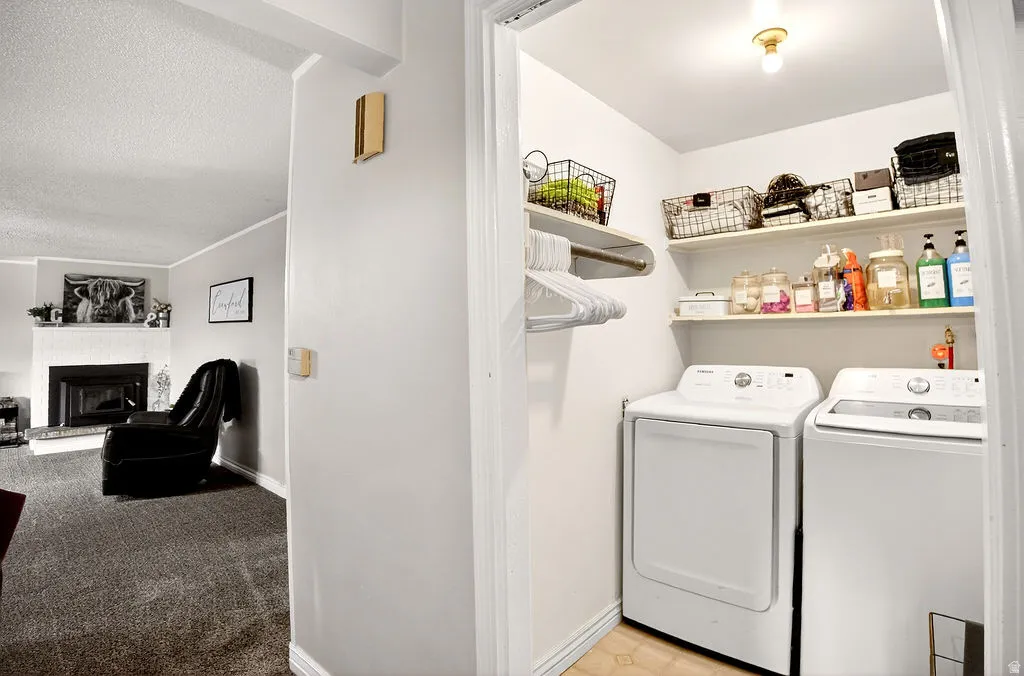 Laundry area with a fireplace with raised hearth, a textured ceiling, independent washer and dryer, light carpet, and ornamental molding