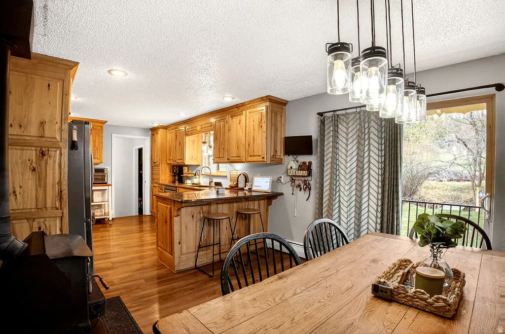 Dining area with a wood stove, a textured ceiling, wood finished floors, and a chandelier