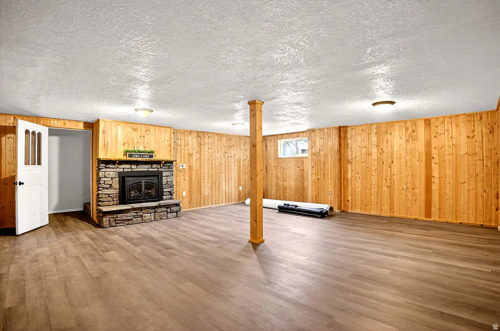 Finished basement with a stone fireplace, wood finished floors, a textured ceiling, and wood walls