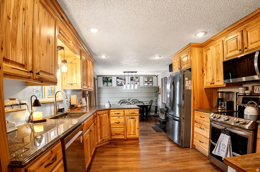 Kitchen featuring stainless steel appliances, a textured ceiling, a peninsula, plenty of natural light, and dark stone countertops