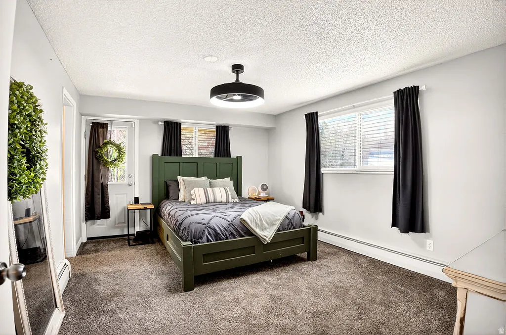Bedroom featuring a baseboard heating unit, carpet floors, and a textured ceiling