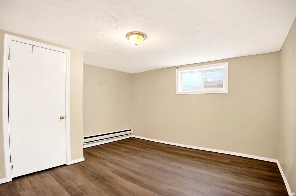 Spare room featuring dark wood finished floors, a textured ceiling, and a baseboard radiator