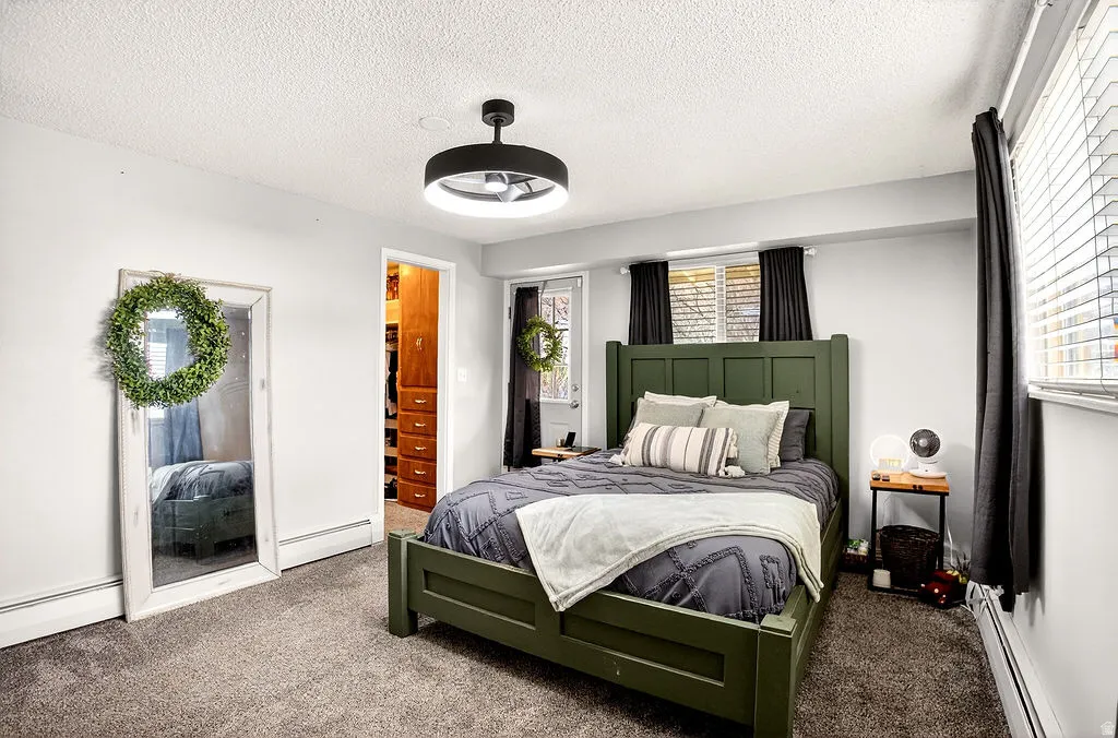 Carpeted bedroom featuring a spacious closet, a textured ceiling, and baseboard heating