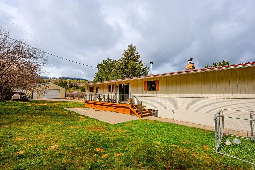 Back of house with a yard, an outdoor structure, a garage, brick siding, and a wooden deck