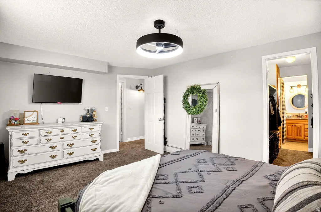 Bedroom featuring dark carpet, a textured ceiling, connected bathroom, and a ceiling fan