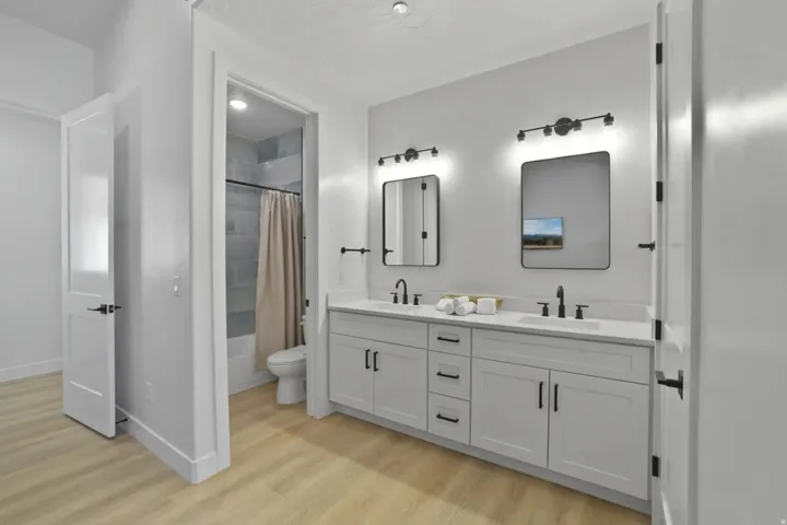 Bathroom with double vanity, light wood-style flooring, and shower / bath combo with shower curtain