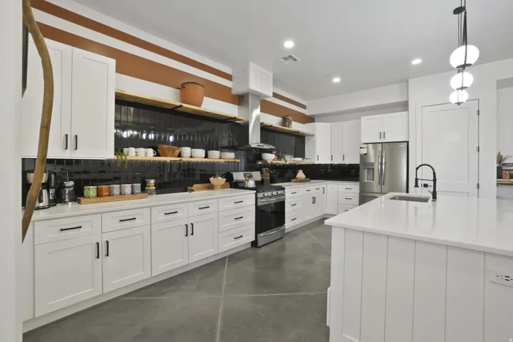 Kitchen featuring decorative backsplash, open shelves, finished concrete flooring, stainless steel appliances, and white cabinets