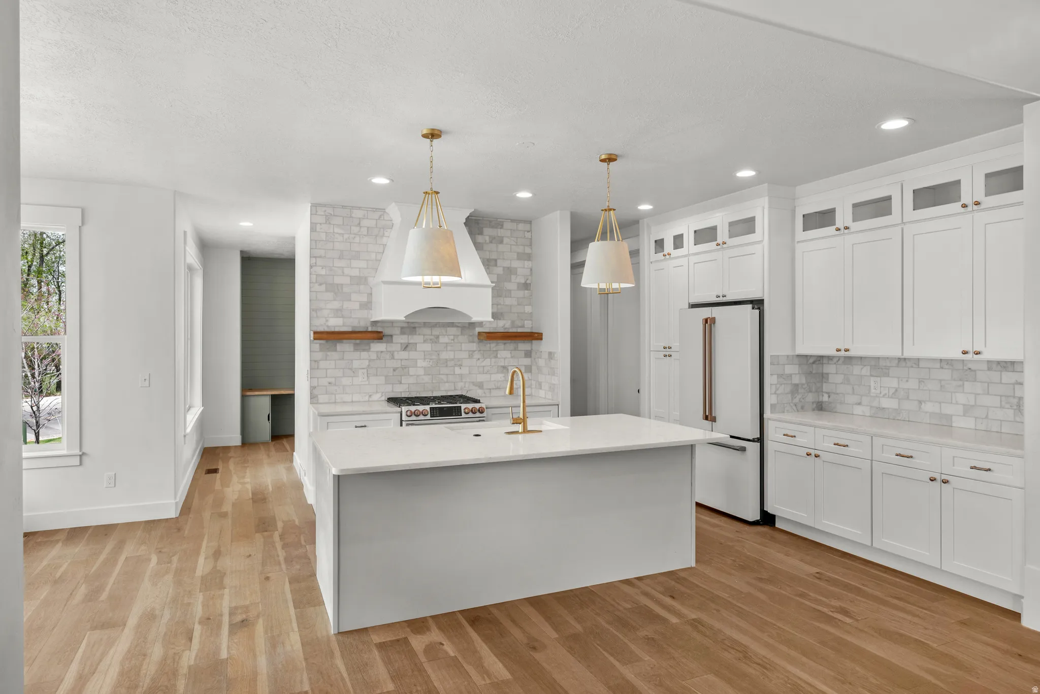 Kitchen with open shelves, pendant lighting, glass fronted cabinets, premium appliances, and a center island with sink