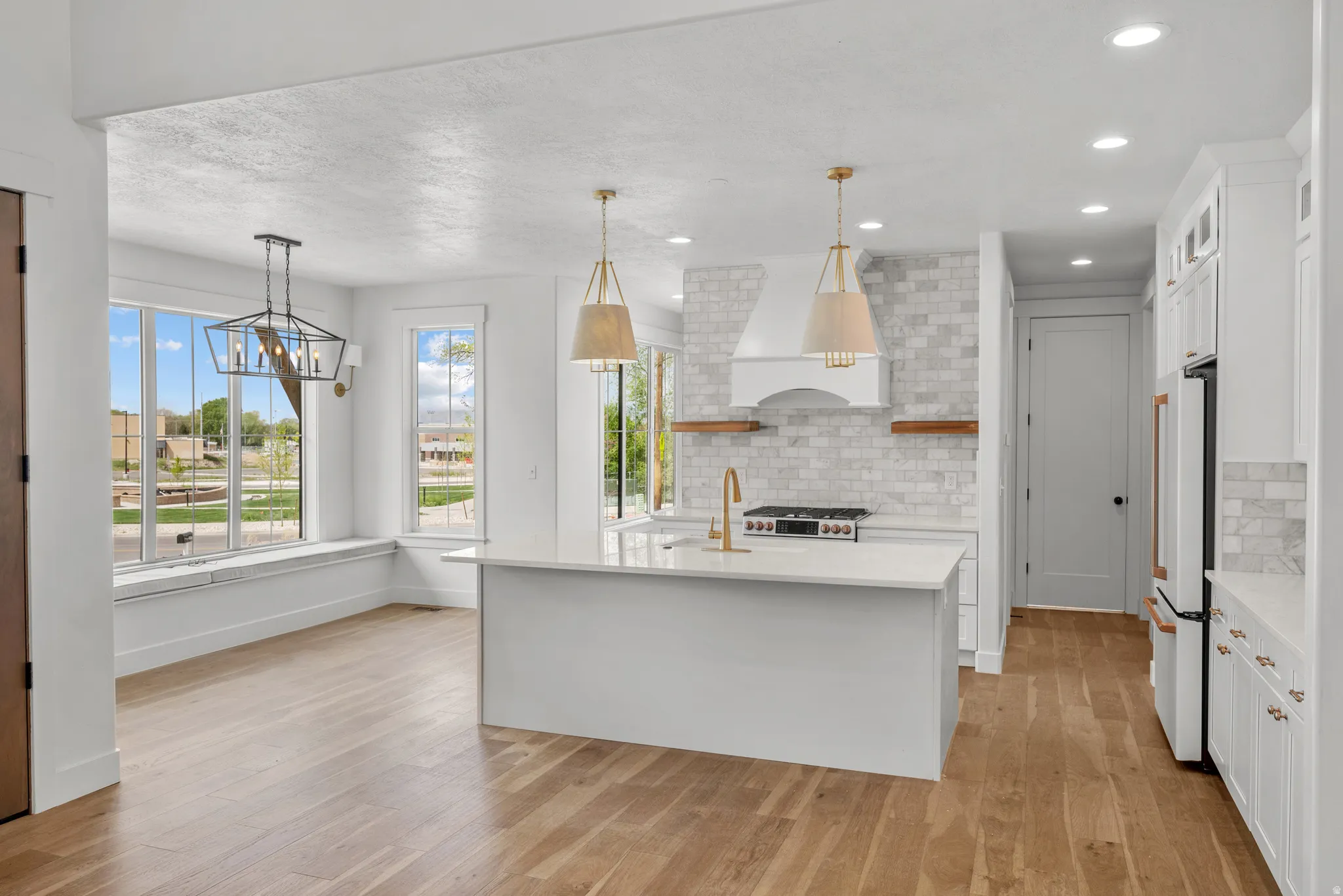 Kitchen featuring open shelves, a kitchen island with sink, white cabinets, backsplash, and light wood-type flooring