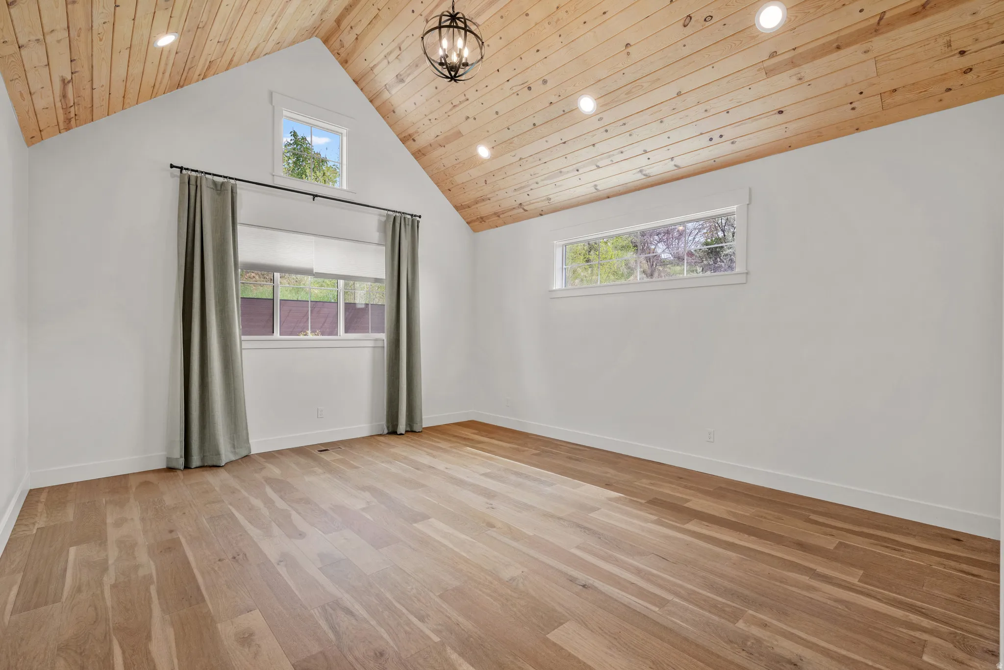 Unfurnished room featuring light wood-style floors, hanging lights, and a high wooden ceiling