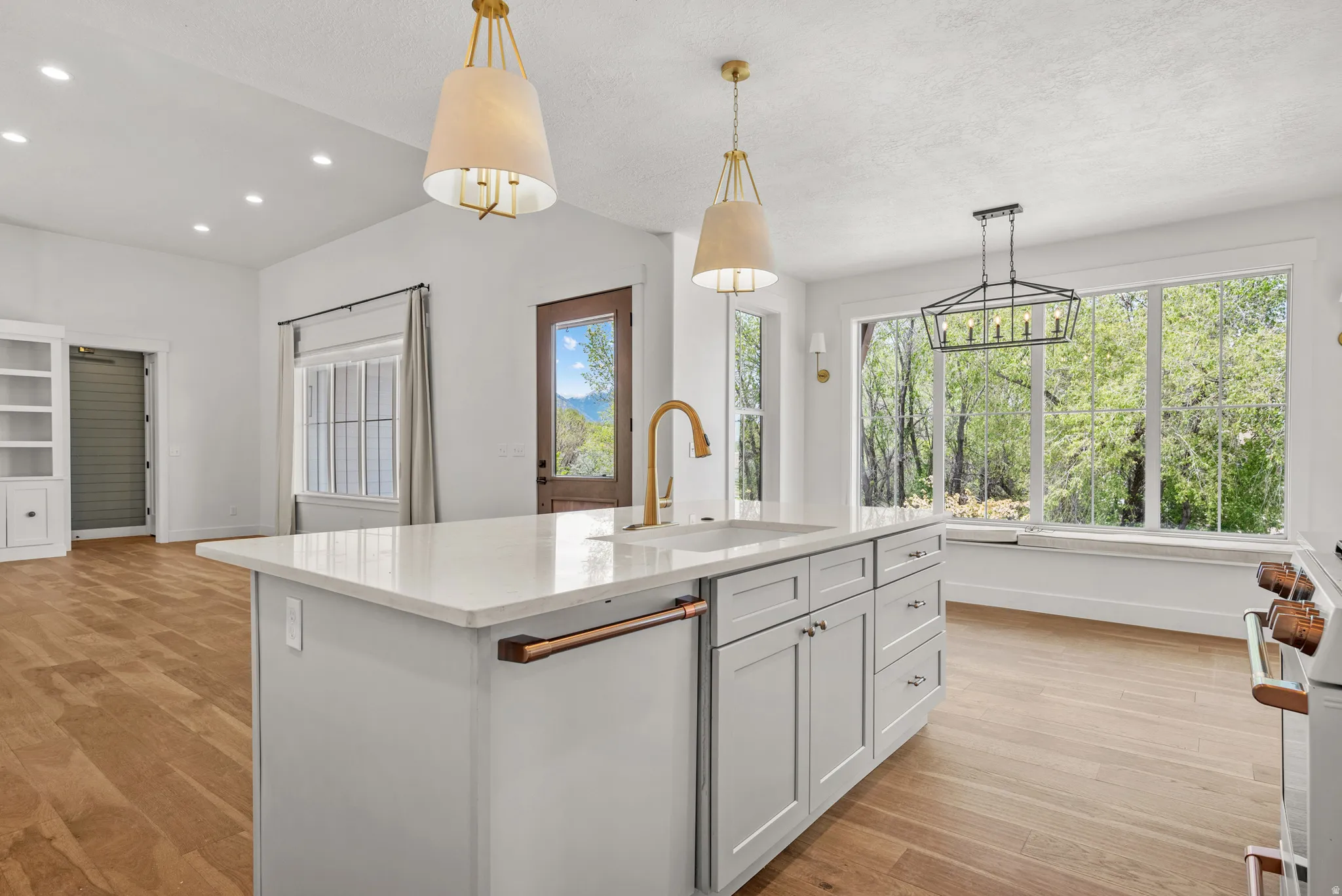 Kitchen featuring light stone counters, light wood finished floors, stove, a center island with sink, and a textured ceiling