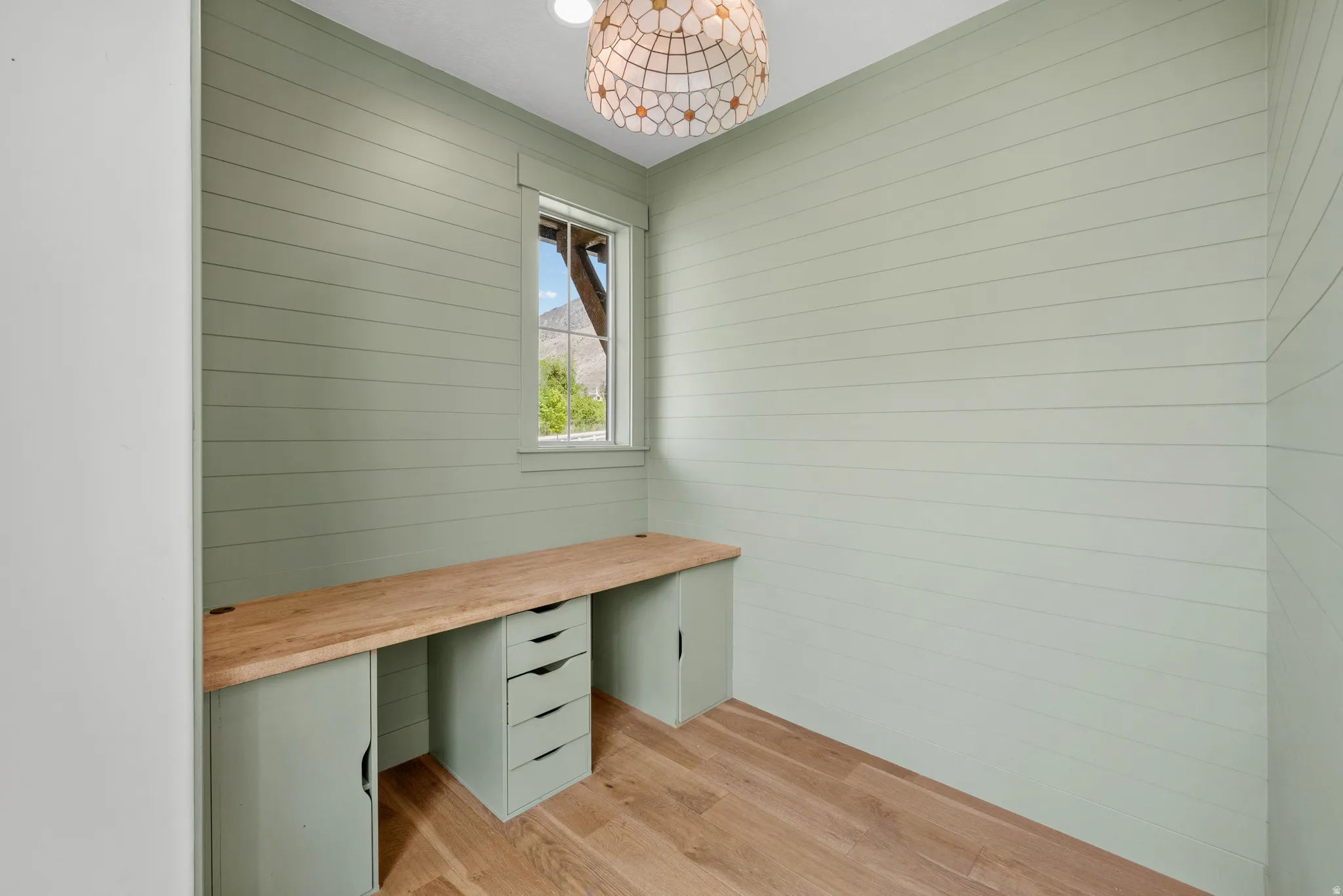 Unfurnished office with light wood-style flooring, wooden walls, and built in study area