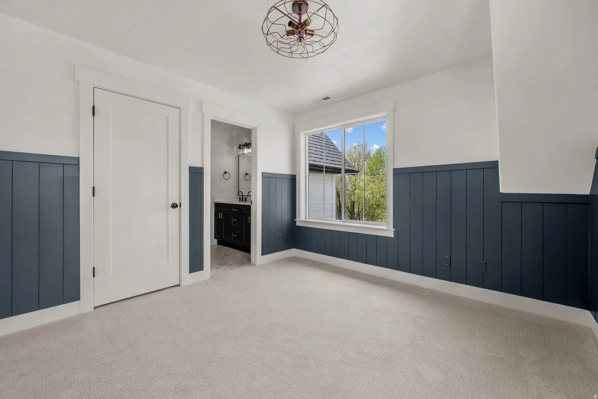 Unfurnished bedroom with a wainscoted wall, ensuite bath, and light carpet