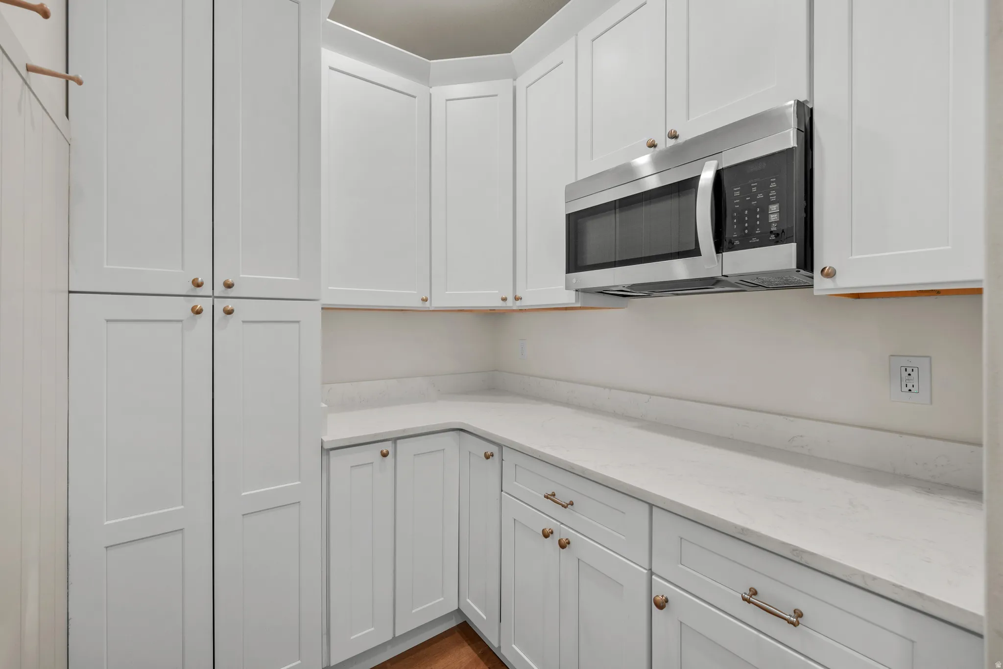 Kitchen featuring stainless steel microwave, light stone counters, and white cabinetry