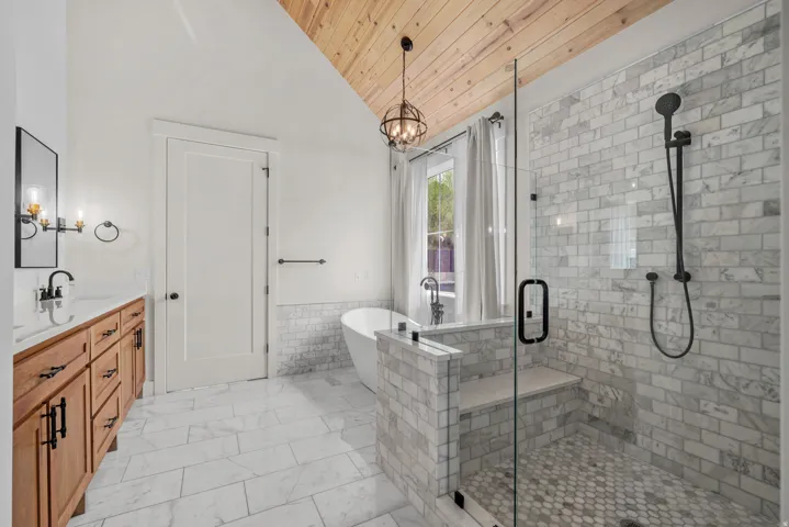 Bathroom featuring double vanity, a freestanding bath, a vaulted wooden ceiling, a shower stall, and a wainscoted wall