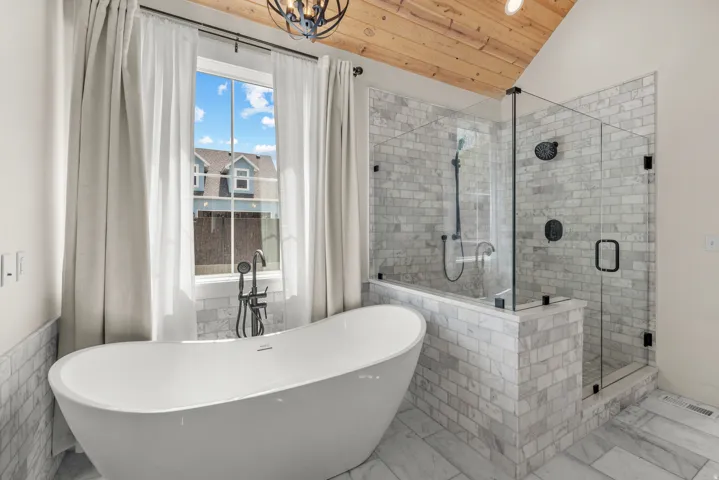 Full bathroom with a shower stall, a freestanding tub, tile walls, a vaulted wooden ceiling, and wainscoting