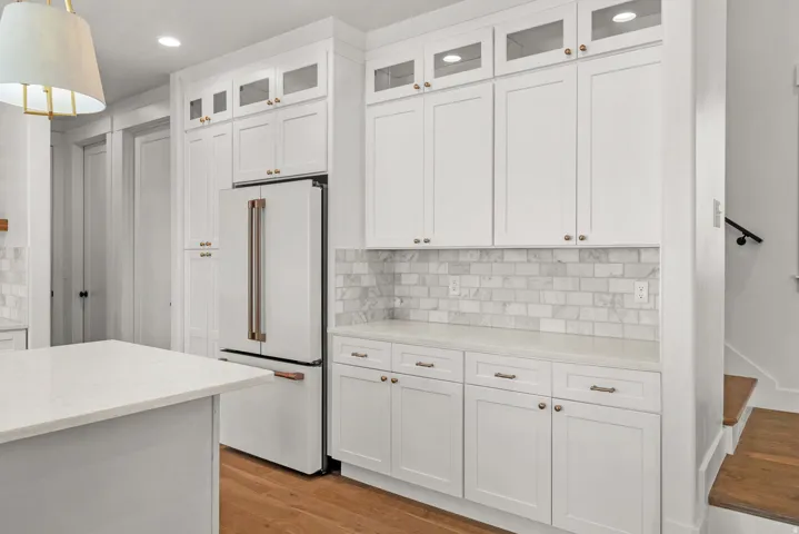 Kitchen with glass insert cabinets, high end white fridge, light stone countertops, and white cabinets
