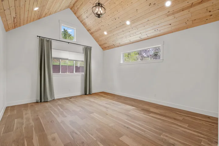 Unfurnished room featuring light wood-style floors, hanging lights, and a high wooden ceiling