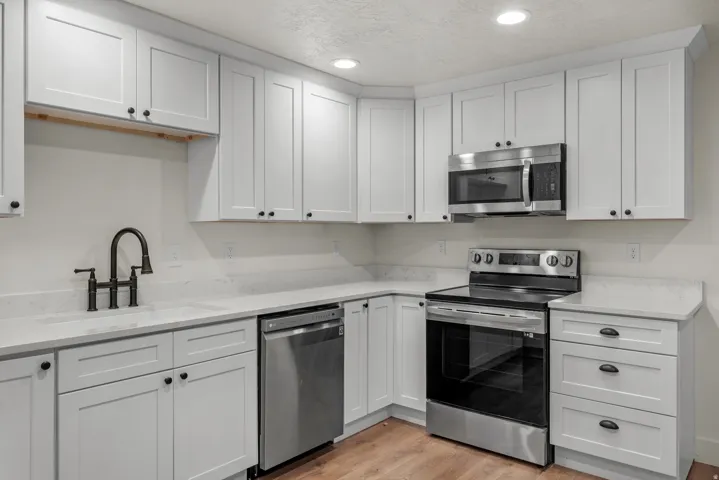 Kitchen with stainless steel appliances, light stone counters, white cabinets, recessed lighting, and a textured ceiling