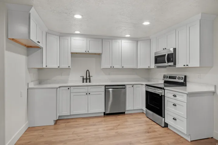 Kitchen with stainless steel appliances, a textured ceiling, recessed lighting, light wood-style flooring, and white cabinetry