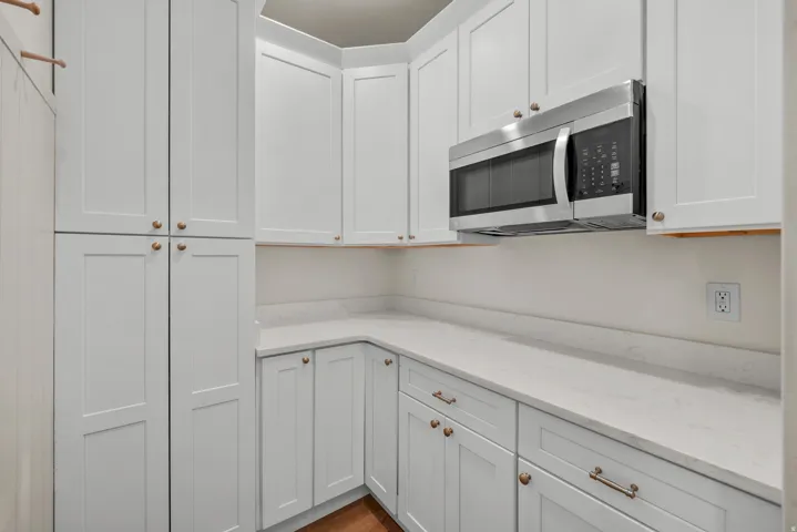 Kitchen featuring stainless steel microwave, light stone counters, and white cabinetry