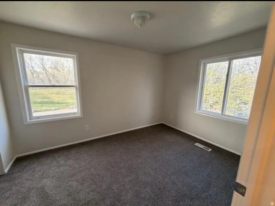 Empty room featuring dark carpet and baseboards