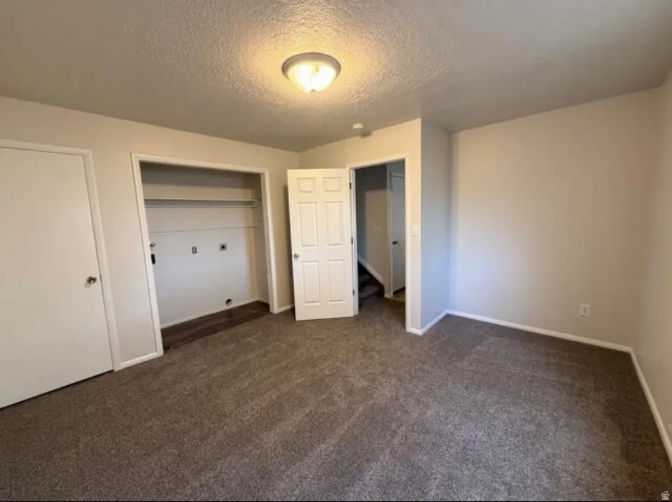 Unfurnished bedroom with dark carpet, a textured ceiling, and a closet