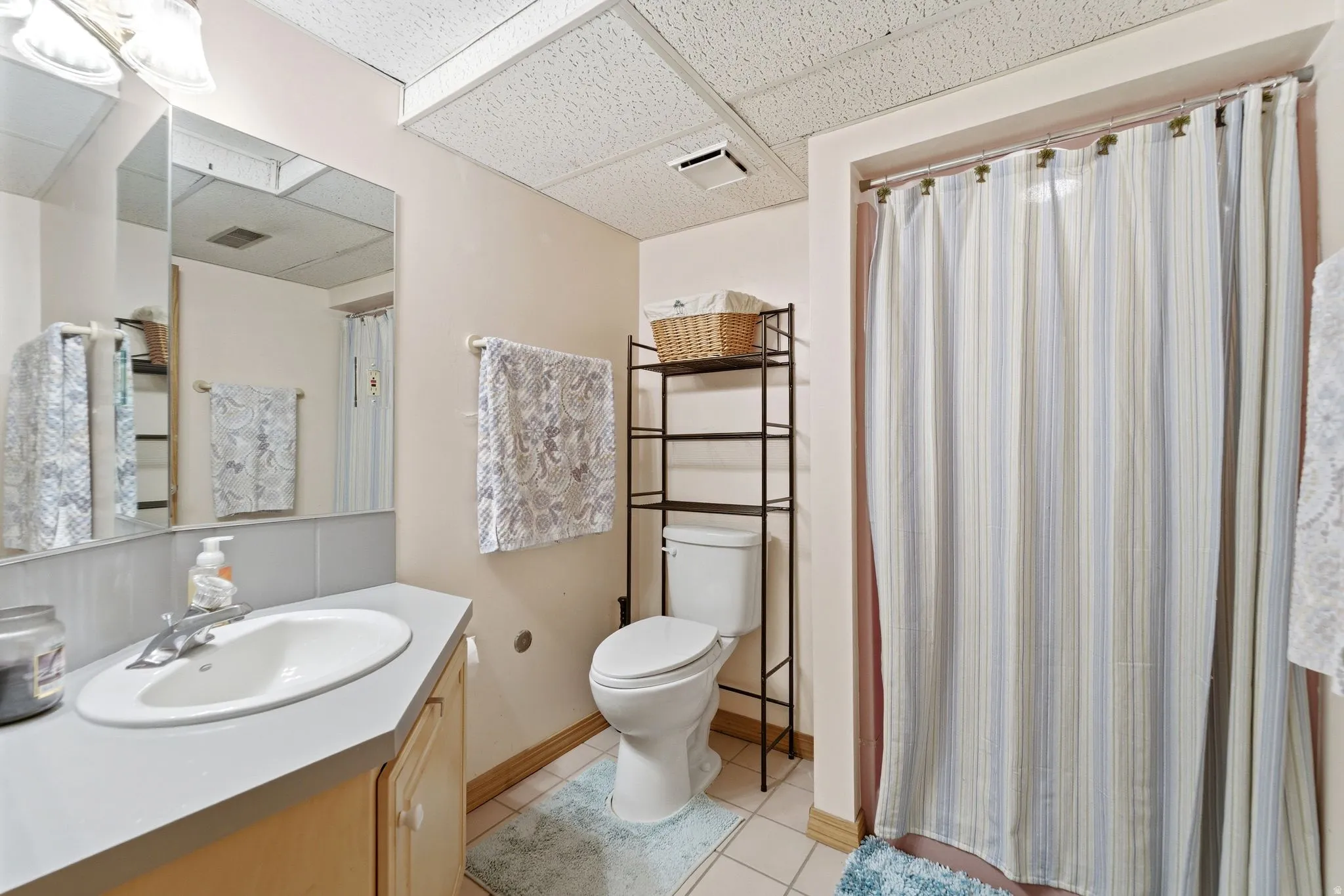 Full bath with vanity, a shower with shower curtain, a drop ceiling, and light tile patterned flooring