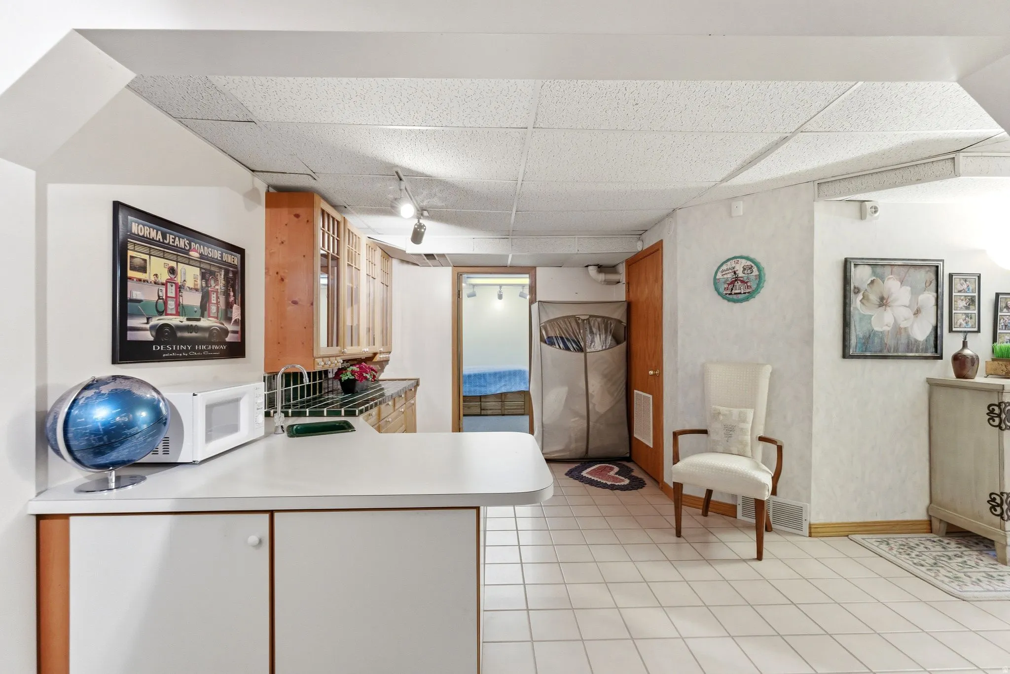 Kitchen featuring a peninsula, a paneled ceiling, light countertops, white microwave, and light tile patterned floors