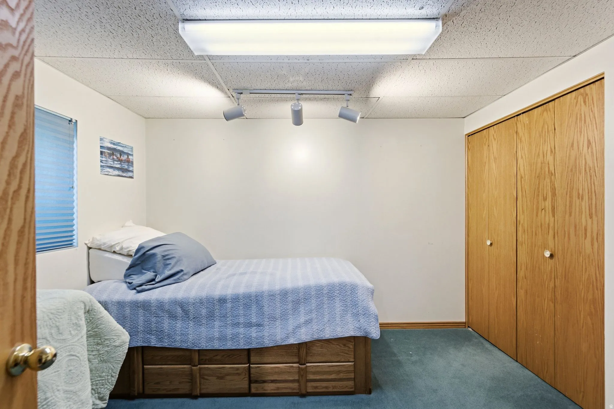 Bedroom with dark carpet, track lighting, a paneled ceiling, and a closet