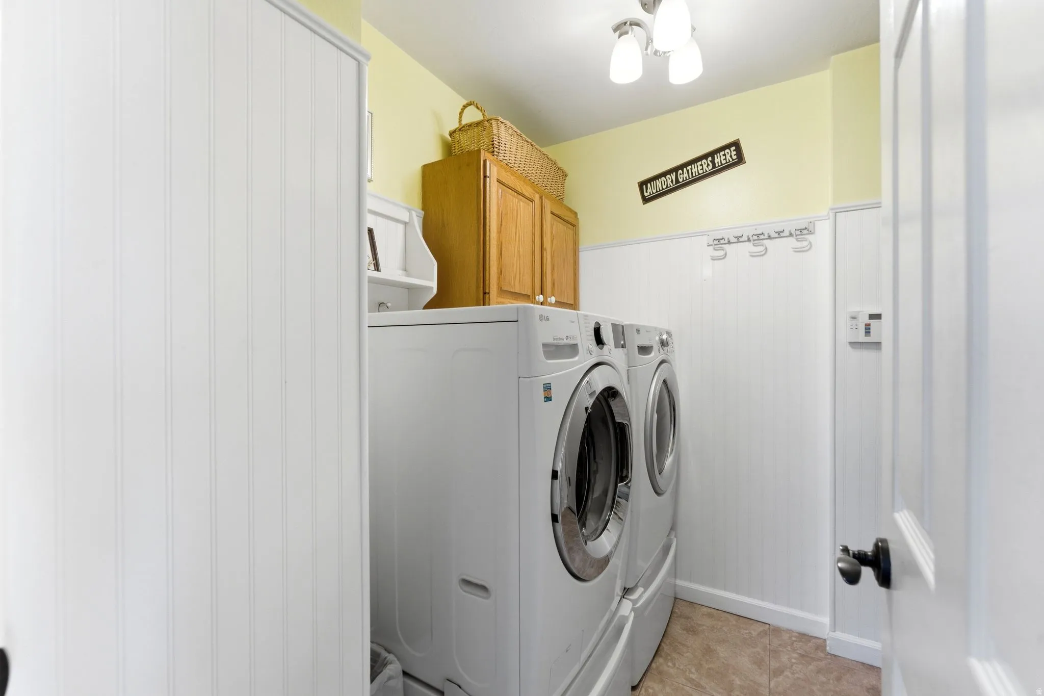 Laundry room featuring cabinet space, washer and dryer, wainscoting, and light tile patterned flooring