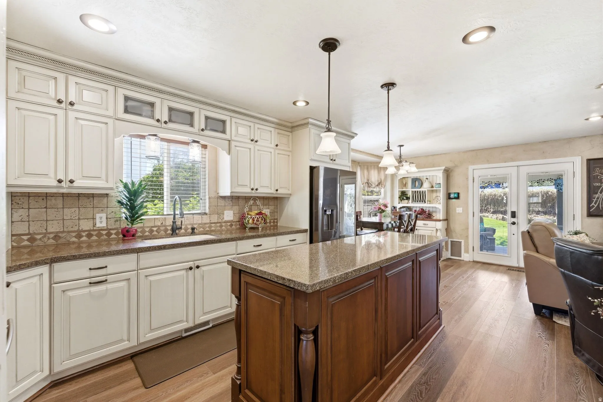 Kitchen with light wood finished floors, hanging light fixtures, two tone cabinets, a kitchen island, and stainless steel fridge with ice dispenser