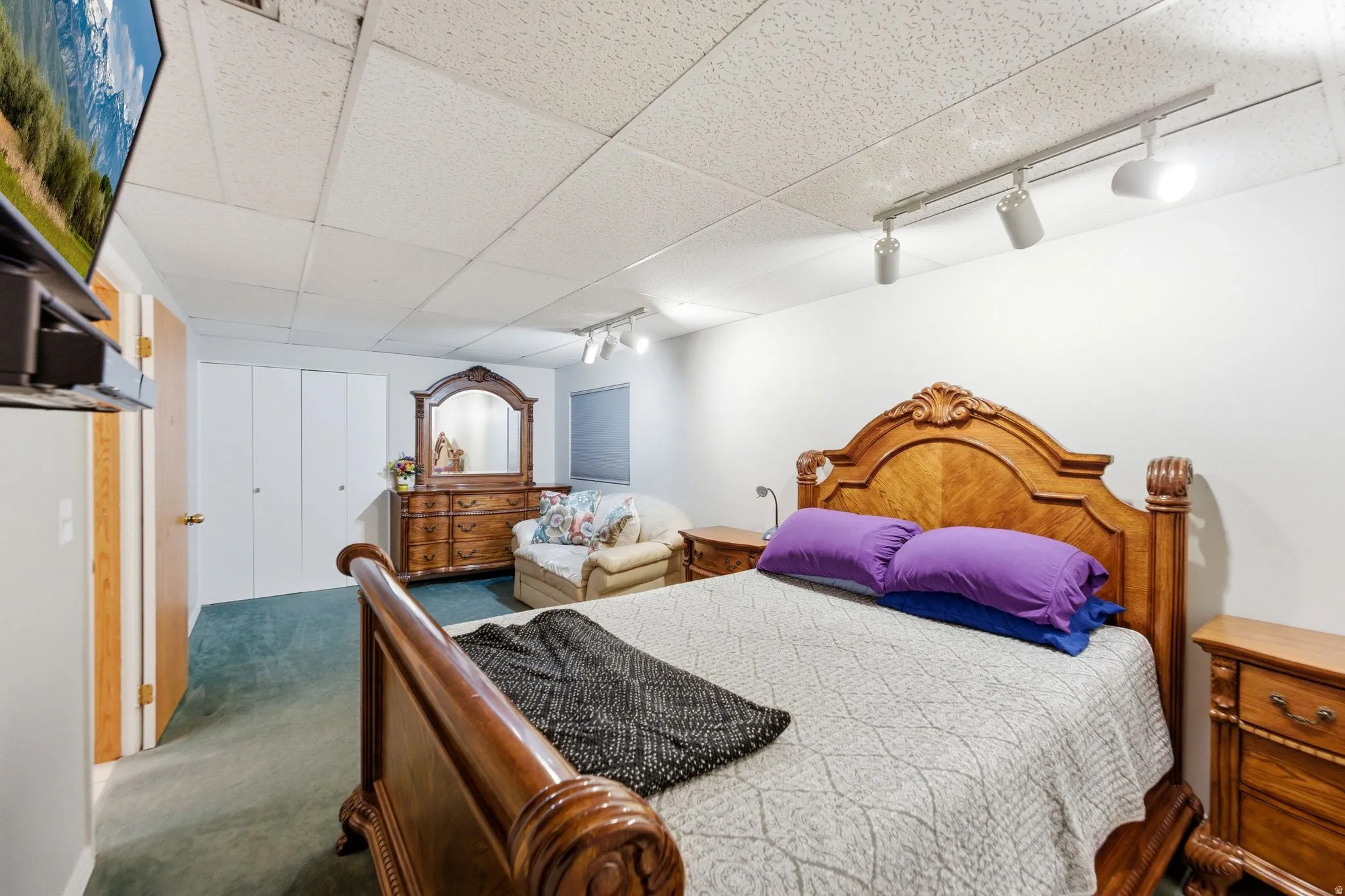 Bedroom featuring rail lighting, a drop ceiling, a closet, and dark colored carpet