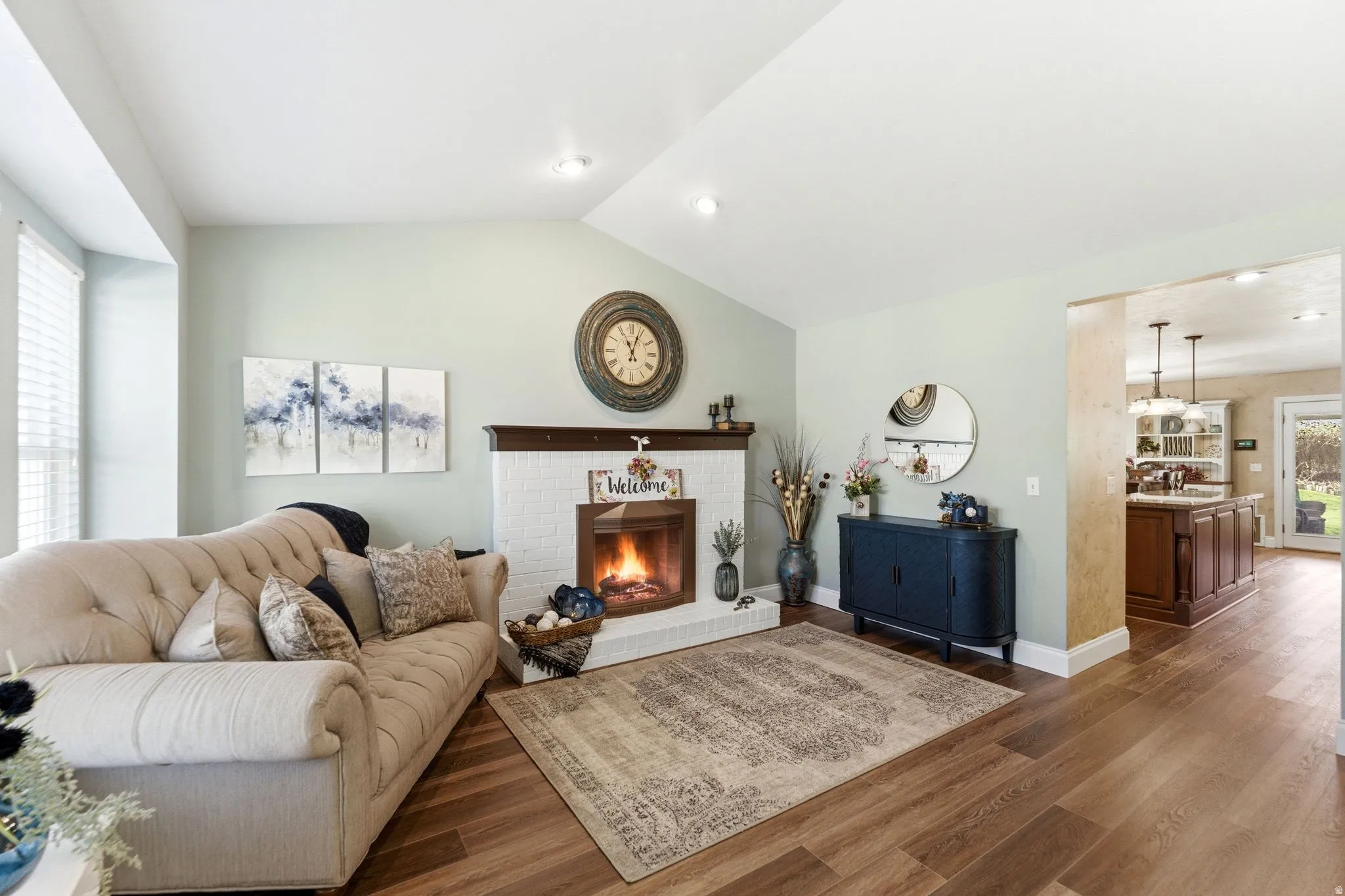 Living room featuring vaulted ceiling, dark wood-type flooring, and a brick fireplace