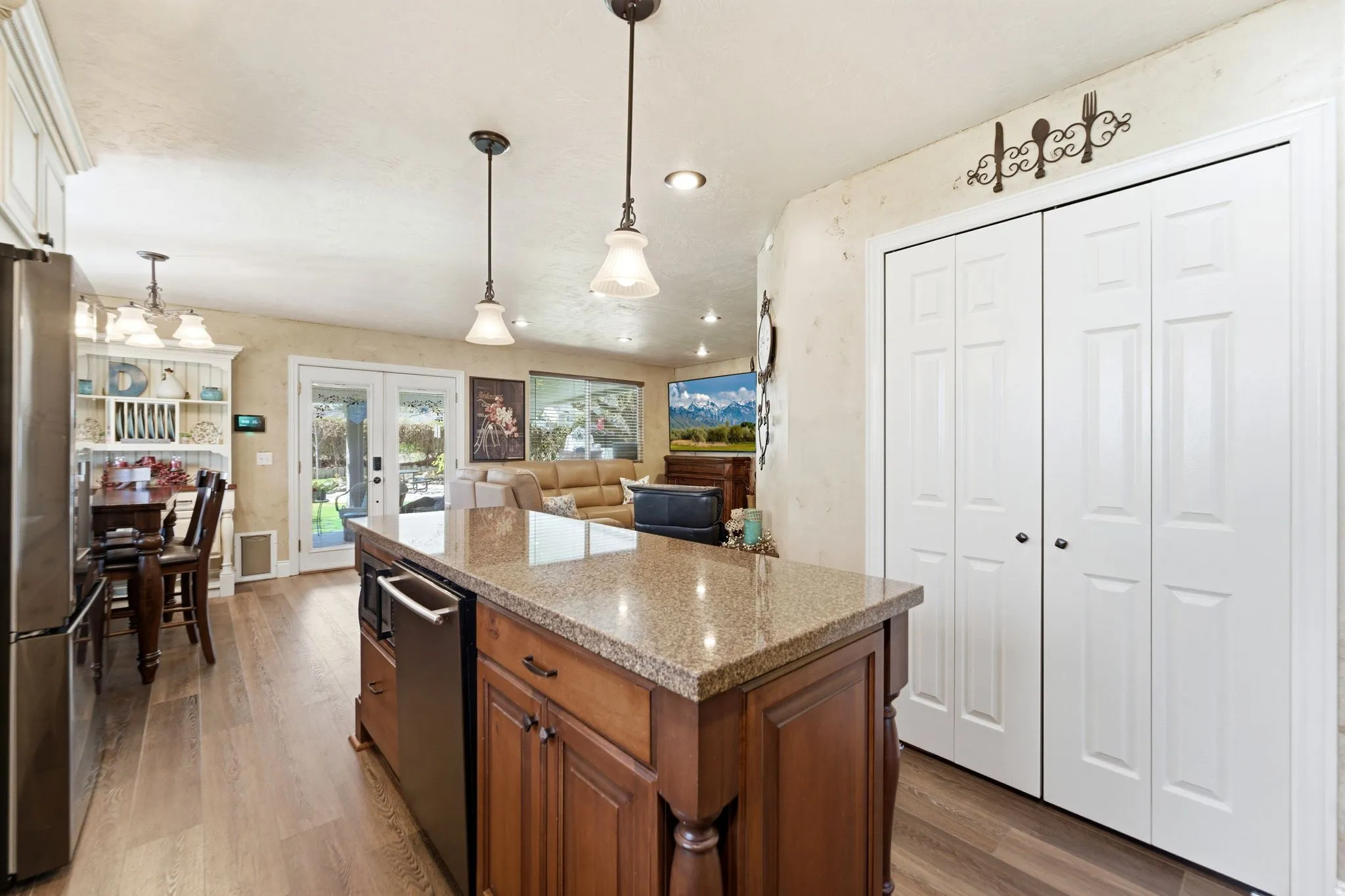Kitchen featuring light stone counters, light wood-style floors, hanging light fixtures, and stainless steel appliances
