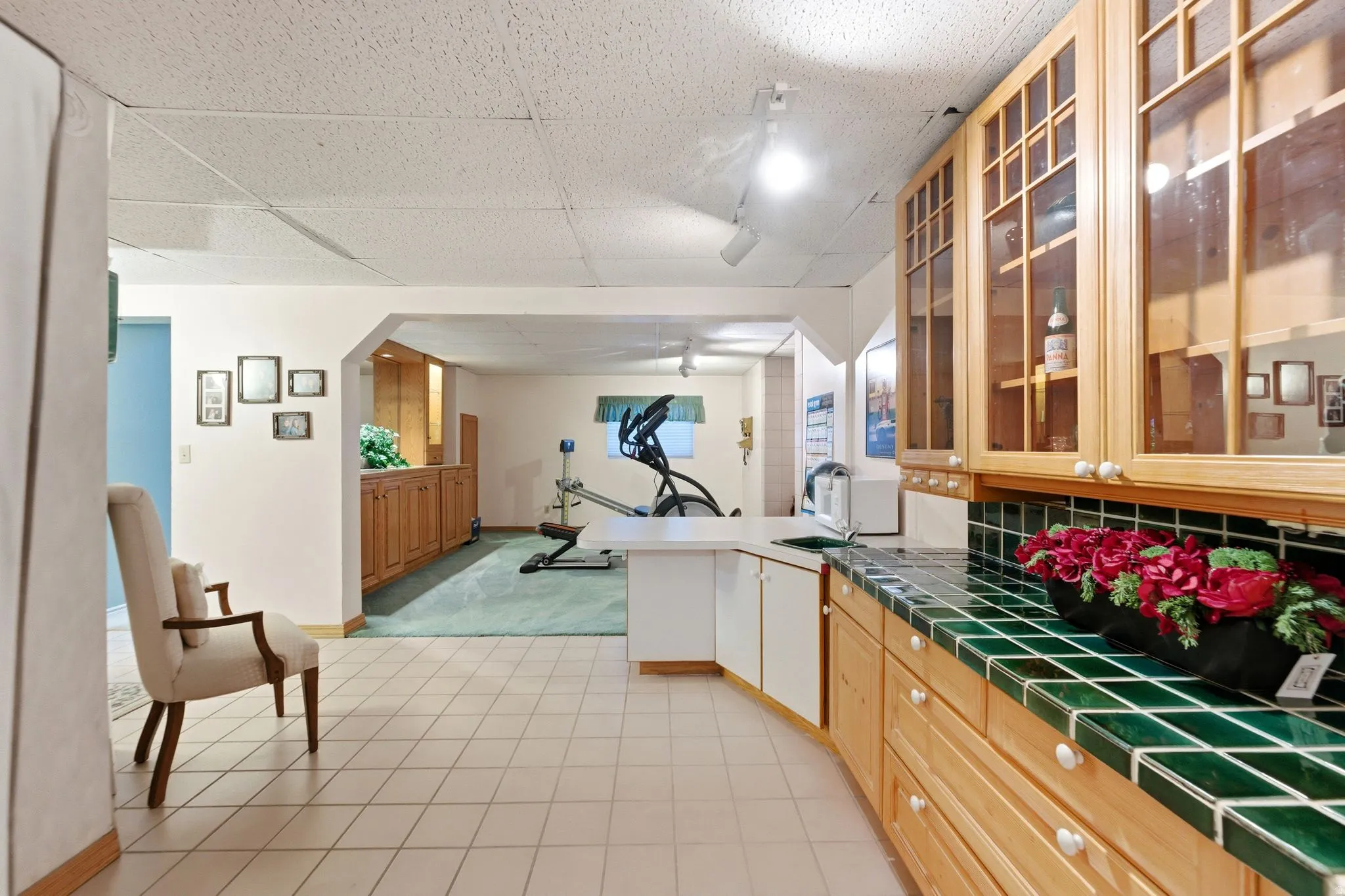 Kitchen with glass insert cabinets, a peninsula, tile counters, a drop ceiling, and light colored carpet