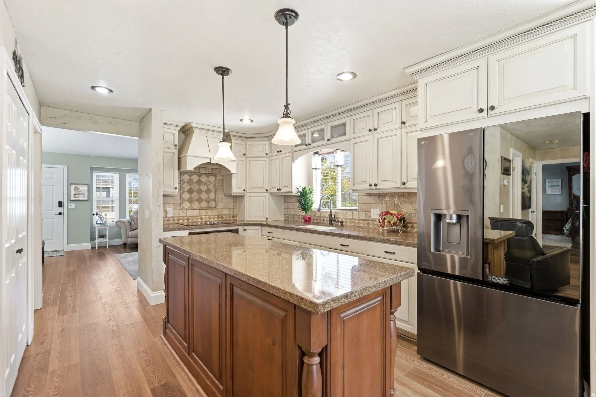Dual tone kitchen featuring stainless steel fridge with ice dispenser, light stone counters, light wood finished floors, a center island, and pendant lighting