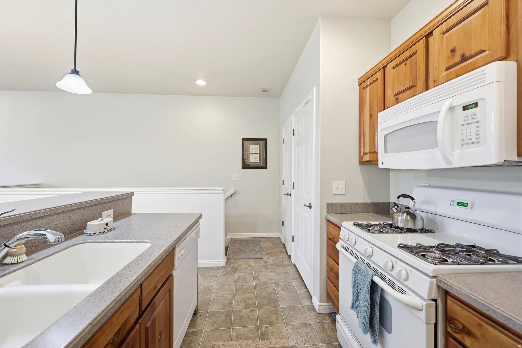 Kitchen featuring white appliances, wood finish cabinetry, and hanging light fixtures