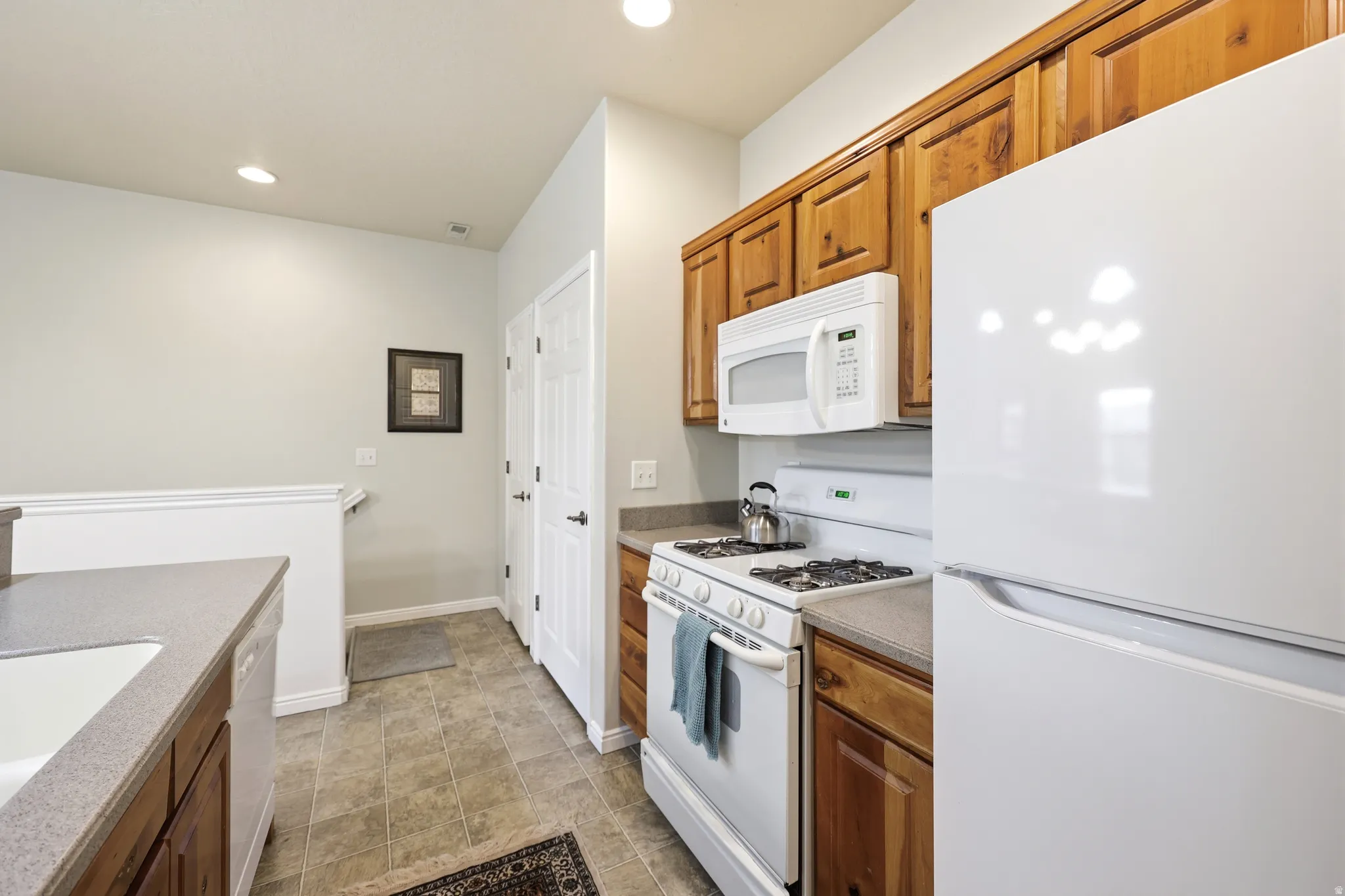 Kitchen with white appliances, wood finish cabinets, recessed lighting, and dark stone countertops