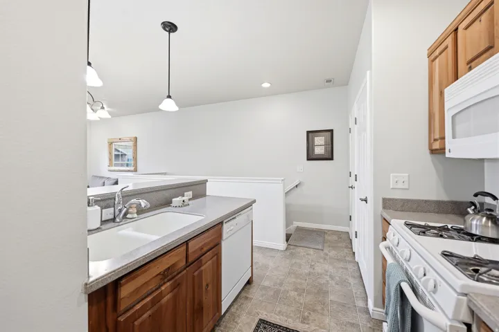 Kitchen featuring white appliances, pendant lighting, wood finish cabinets, and light countertops