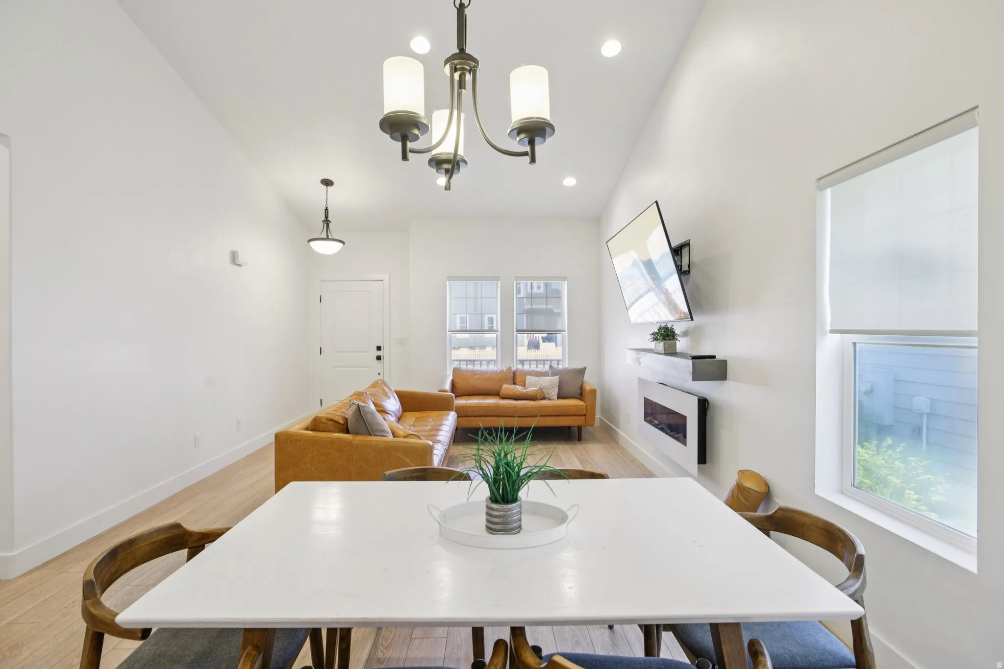 Dining area with a glass covered fireplace, light wood-style floors, hanging lights, and lofted ceiling