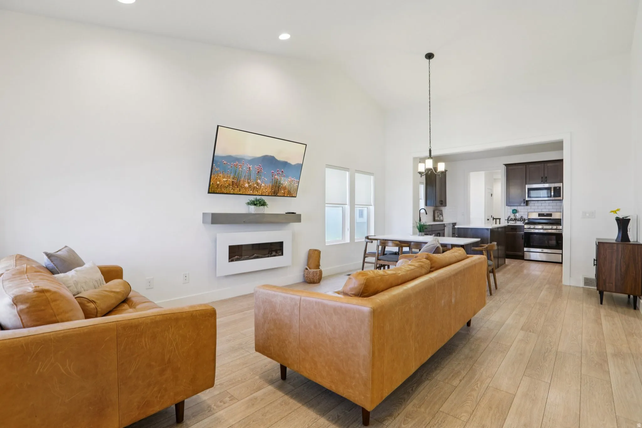Living room with a glass covered fireplace, light wood-style flooring, hanging lights, and vaulted ceiling